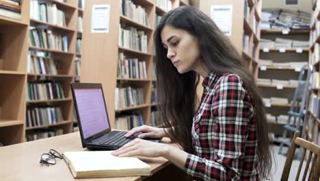 Chica-estudiante-en-una-biblioteca-universitaria-sentada-con-ordenador-portátil