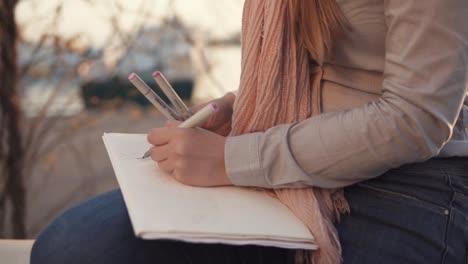 Woman-is-drawing-sketches-of-landscape-in-open-air-in-evening,-close-up-of-hands