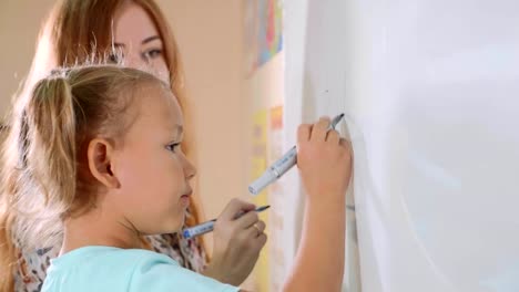 Niña-linda-con-profesor-escribiendo-en-la-pizarra-en-clase