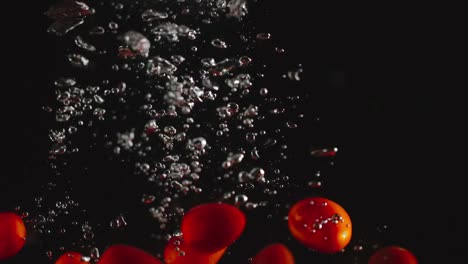 SLOW-MOTION:-Cherry-tomatoes-fall-under-water-on-black-background