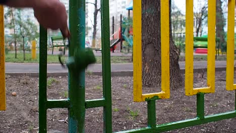 Ein-Arbeiter-grüne-Farbroller-Malerei-einen-gelb-grünen-Zaun-auf-dem-Hintergrund-Spielplatz