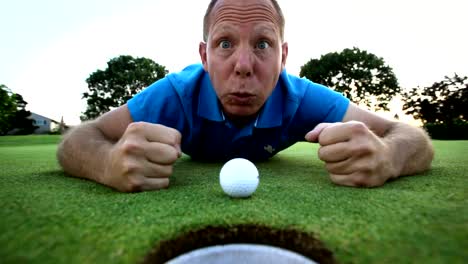 Golfer-lays-down-and-tries-to-blow-his-ball-into-the-hole.-Close-up-shot.