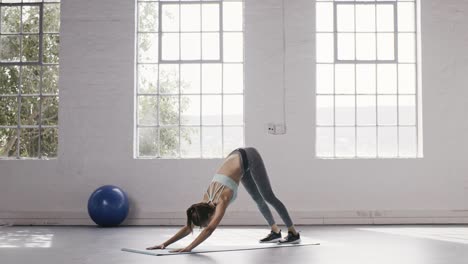 Woman-doing-one-legged-down-dog-pose-in-yoga-studio