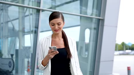 Hermosa-mujer-con-teléfono-caminando-cerca-de-oficina-de-negocios