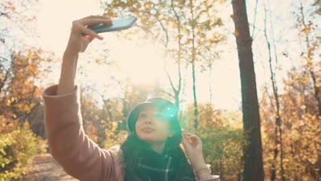 Reizendes-Mädchen-nimmt-Selfie-mit-dem-Handy-in-sonnigen-herbstlichen-Wald,-Lächeln