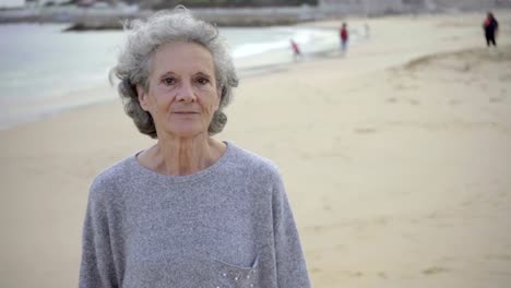 Smiling-senior-woman-walking-on-sandy-beach-and-talking-to-camera.