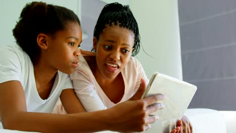 Front-view-of-mid-adult-black-mother-and-daughter-using-digital-tablet-on-bed-in-comfortable-home-4k