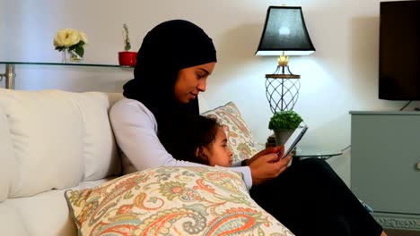 Young-mother-using-a-digital-tablet-with-her-daughter-on-the-sofa-at-home-4k