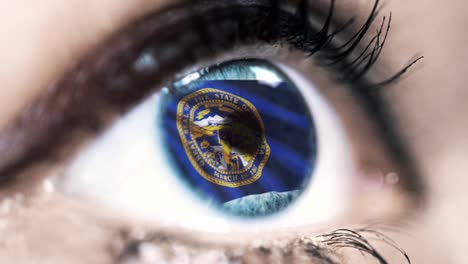 Woman-blue-eye-in-close-up-with-the-flag-of-Nebraska-state-in-iris,-united-states-of-america-with-wind-motion.-video-concept