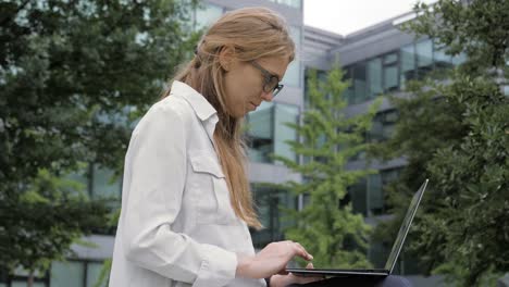 Junge-Geschäftsfrau-mit-tragbaren-Computer-in-grünen-Park-am-Bürogebäude