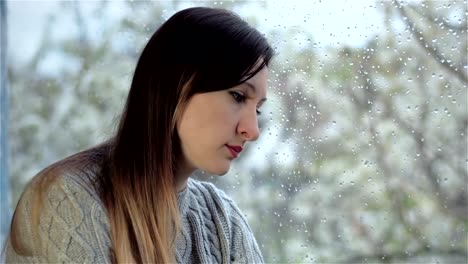 Triste-mujer-apoyó-su-mejilla-contra-la-ventana-húmeda.-Cierre-para-arriba