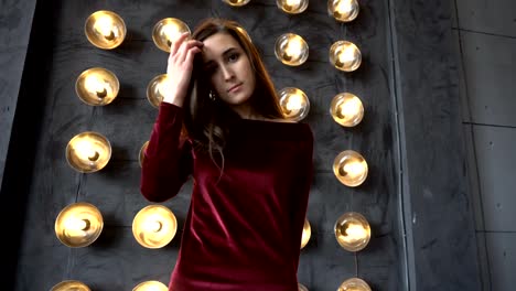 Young-woman-in-dress-and-beautiful-face-on-a-background-of-wall-with-powerful-lamps