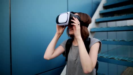 Zukunft-ist-jetzt.-Schöne-junge-Frau-auf-einer-Treppe-Rollenspiel-in-Vr-Brille.-Kaukasische-Mädchen-berühren-etwas-mit-modernen-virtual-Reality-Brille-auf-blauem-Grund.