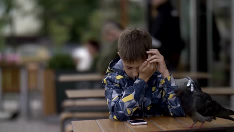 boy-with-a-school-backpack-sleeping-sitting-at-a-table-in-a-cafe-outdoors