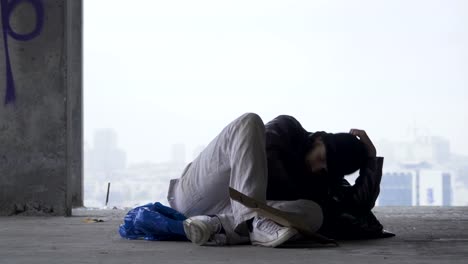 Homeless-man-goes-to-sleep-on-the-garbage-bag,-urban-background