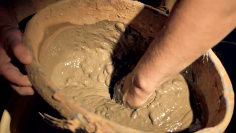 Potter-mixes-clay-by-hand-in-a-pail.