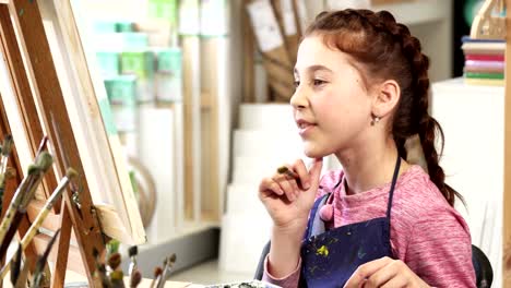 Cute-little-girl-showing-thumbs-up-while-painting-a-picture-at-the-art-class