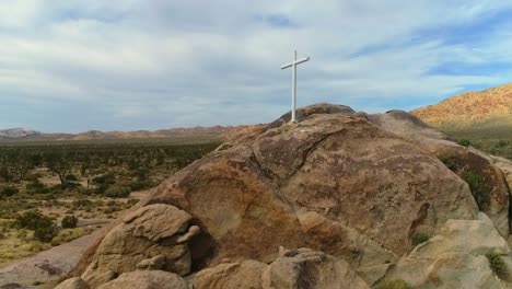 aerial-view-over-a-desert-highway-ending-with-a-white-cross-on-top-of-a-mountain