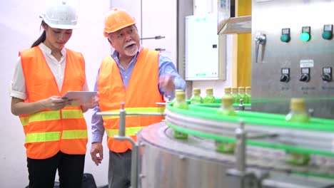 Senior-quality-inspector-teaching-junior-team-member-in-factory.-Chinese-old-male-with-his-young-team-discussing-quality-issue-with-bottle-production-line-in-background.