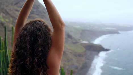 Mujer-joven-haciendo-yoga-en-la-montaña-en-una-isla-con-vista-al-mar,-sentada-en-una-piedra-en-la-cima-de-una-montaña-meditando-en-posición-de-loto