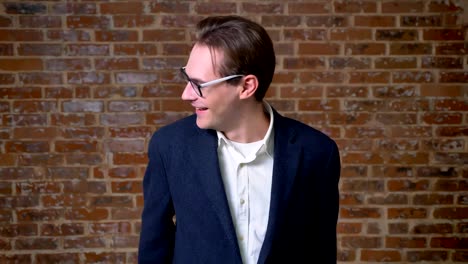 Chill-caucasian-businessman-is-laughing-next-to-camera-in-motion-standing-in-same-position,-brick-background