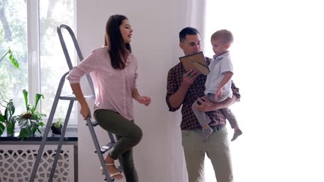 renovation-teamwork-of-flat,-happy-family-with-child-doing-repairs-in-apartment-and-hang-painting-using-stepladder-at-home