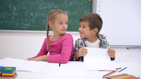 compañeros-de-clase-los-niños-abrazando-sonriente-sentada-en-el-escritorio-en-el-fondo-de-la-pizarra-en-clase-en-la-escuela