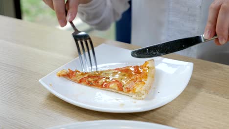 Corte-un-pedazo-de-pizza-con-cuchillo-y-el-tenedor-en-un-plato-blanco