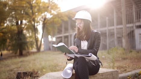 The-woman-student-architect-on-a-construction-site-examines-the-technical-documentation-and-makes-notes-in-his-notebook