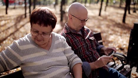 Una-pareja-de-ancianos-en-otoño-parque-en-un-banco-tomando-fotos-de-mí-mismo-en-el-teléfono-inteligente.