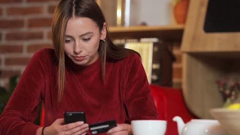 Mujer-joven-haciendo-compra-tarjeta-de-crédito-en-línea,-escribir-los-datos-en-smartphone-negro-en-la-cocina-moderna