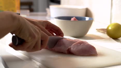 Close-up-Frau-schneidet-Huhn-mit-einem-Messer-auf-einem-Brett.-Weibliche-Hände-Koch-schneiden-rohes-Fleisch-Hühnerbrust.