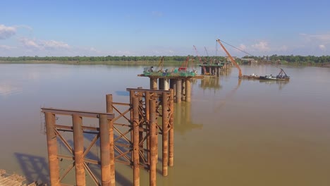 drone-shot:-fly-over-columns-of-new-bridge-under-construction-in-river