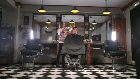 Innenaufnahme-des-Arbeitsprozesses-in-modernen-Friseursalon.-Seite-Ansicht-Porträt-der-attraktive-junge-Mann-immer-trendigen-Haarschnitt.-Männliche-Friseur-servieren-Kunden,-was-Haarschnitt-mit-Metall-Schere-und-Kamm