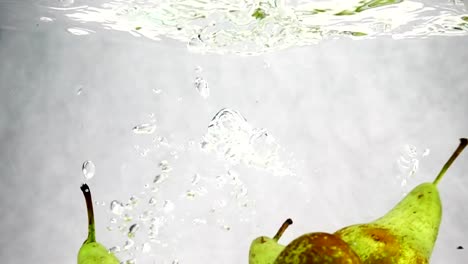 Peras-verdes-cae-al-agua-con-un-montón-de-pequeñas-burbujas.-Video-de-frutas-sobre-fondo-blanco-aislado.