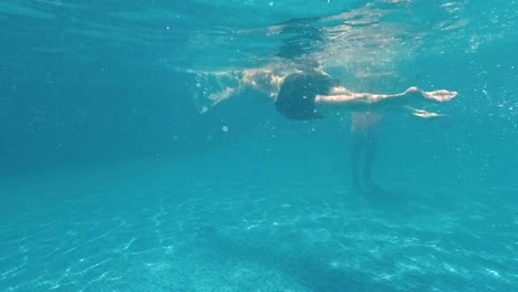 Chico-joven-nada-bajo-el-agua-en-una-piscina