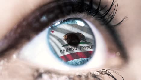 Woman-blue-eye-in-close-up-with-the-flag-of-California-state-in-iris,-united-states-of-america-with-wind-motion.-video-concept