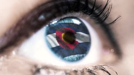 Woman-blue-eye-in-close-up-with-the-flag-of-Colorado-state-in-iris,-united-states-of-america-with-wind-motion.-video-concept