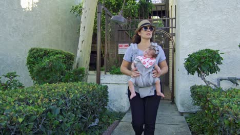 Woman-coming-out-of-building-with-sleeping-baby-on-carrier