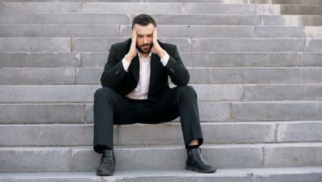 Upset-young-business-man-having-stress-and-sitting-on-stairs-in-street.-Businessman-having-deal-problems-concept