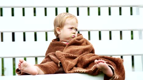 ein-ein-Jahr-alte-Mädchen,-eingewickelt-in-ein-Handtuch-mit-einem-schmutzigen-Gesicht,-einsam-sitzt-auf-einer-Schaukel-im-Garten,-im-Sommer.-Sie-hat-einen-traurigen-Blick.-Sie-will-schlafen