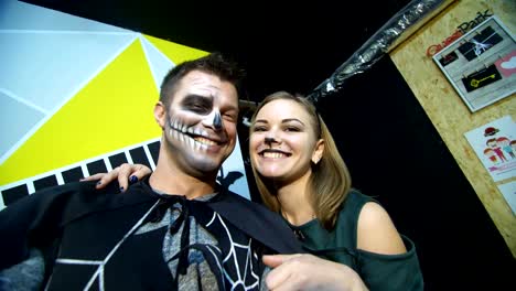 Halloween-party,-night,-frightening-portrait-of-a-man-with-a-terrible-makeup-in-a-black-costume-and-a-girl-in-a-cat-costume,-they-croak-in-front-of-the-camera