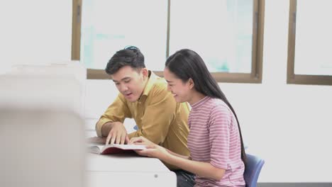 Two-students-sitting-and-reading-book-at-desk.-People-meeting-team-in-the-library-indoors.-Concept-of-education,-together,-teamwork,-learning,-information,-knowledge-and-research.