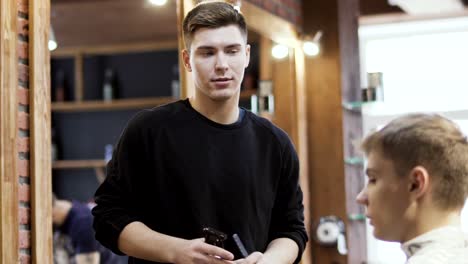 Professional-stylist-cuts-beard-of-young-man-with-electric-razor-in-barbershop