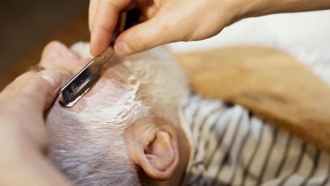 Barber-shaves-beard-of-mature-man-with-sharp-blade