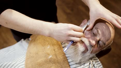 Barber-shaves-beard-of-senior-man-with-blade-in-barbershop