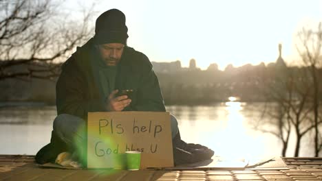 Homeless-man-using-mobile-phone-while-begging