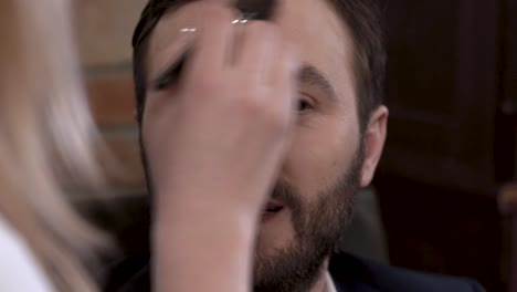 Bearded-man-actor-is-smiling-while-getting-makeup-before-filming.