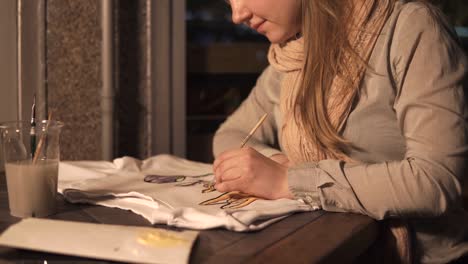 young-artist-is-engaged-in-drawing-on-a-T-shirt-in-her-small-home-workshop