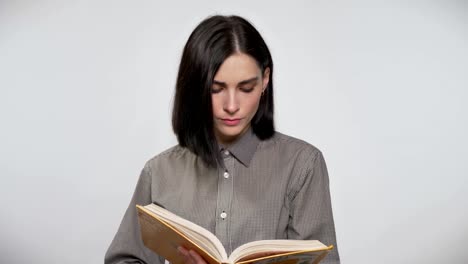 Young-beautiful-woman-with-short-brown-hair-holding-and-reading-book,-concentrated,-white-background